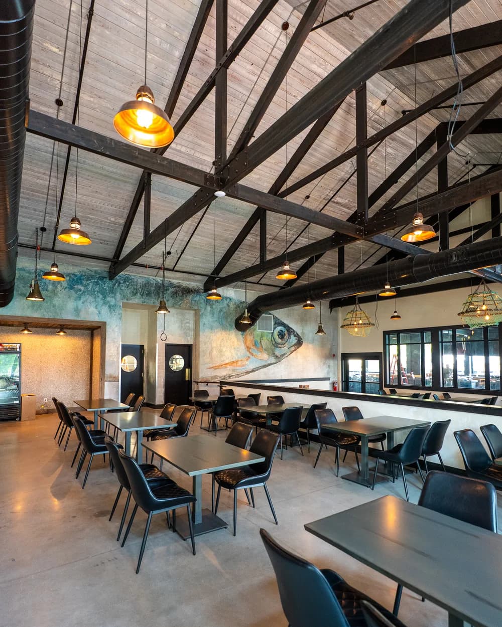 Big Fish dining room with exposed rafters, a fish mural and tables by the windows
